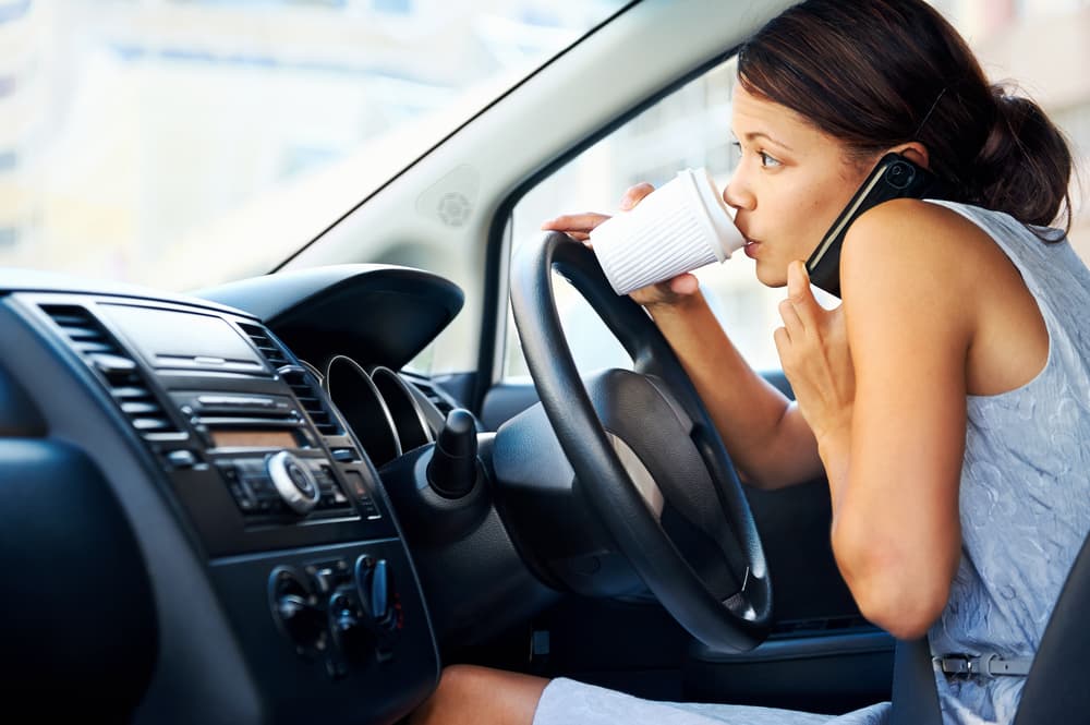 Businesswoman multitasking while driving, drinking coffee and talking on the phone.