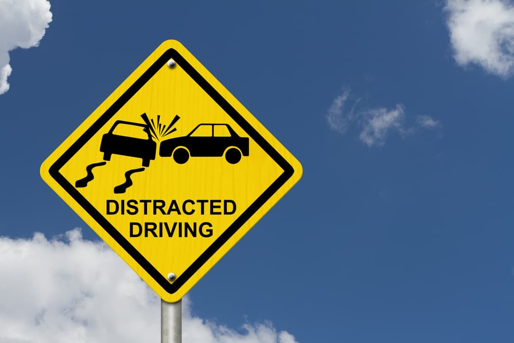 Yellow warning sign with words Distracted Driving and accident icon with sky background.