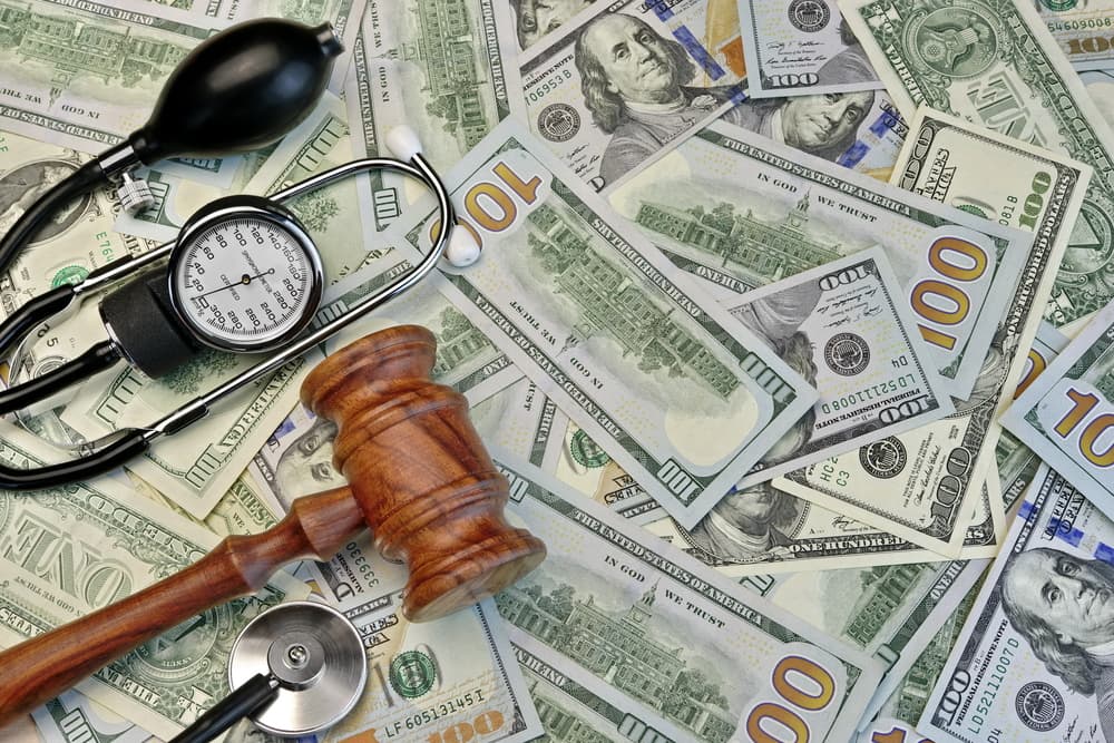 Stethoscope, blood pressure monitor, gavel, and scattered dollars symbolizing healthcare costs and legal issues.