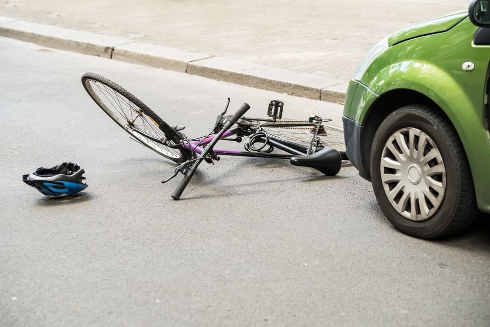 Bicycle and helmet on the road near a green car, depicting a collision aftermath.