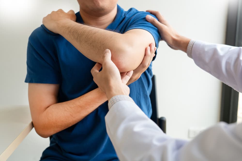 Doctor examining a patient's injured elbow, assessing mobility and pain in a clinical setting.