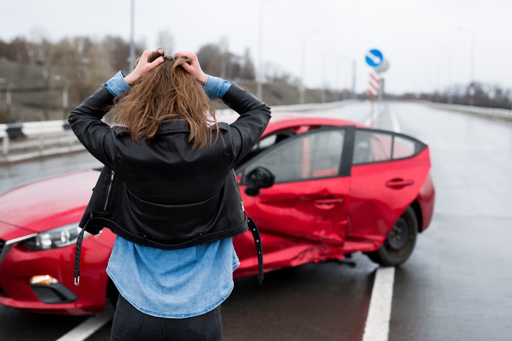 Woman stands near a broken car after an accident.