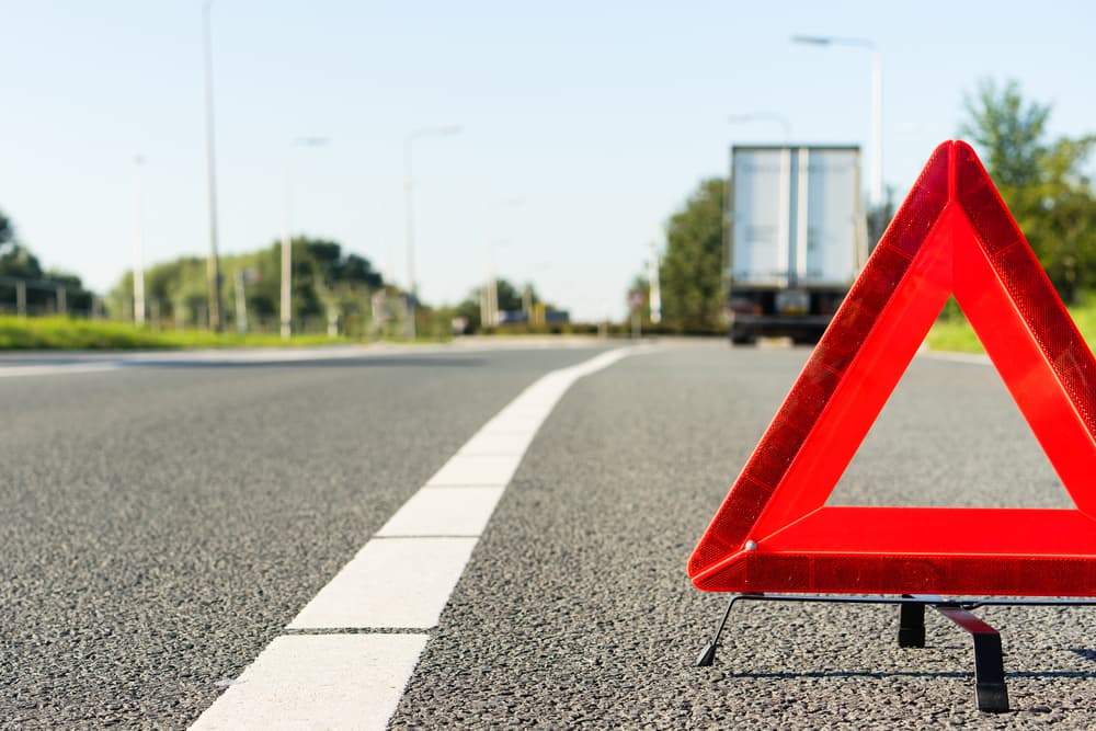 Red warning triangle on a highway signaling danger with a truck in the background.
