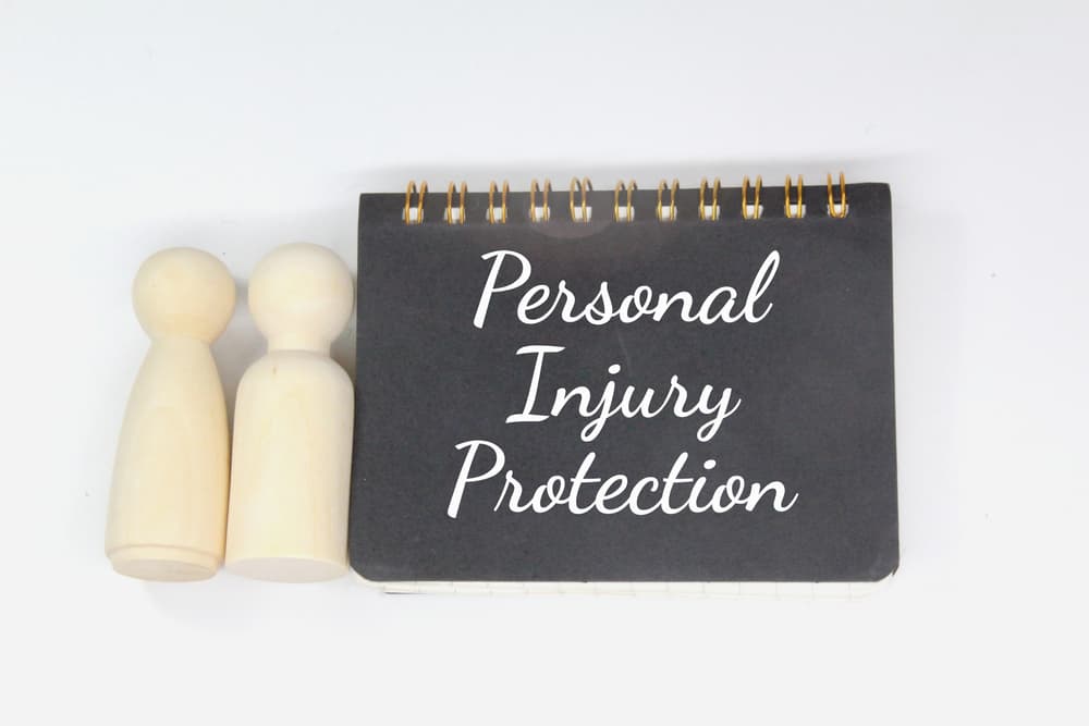 Notebook labeled "Personal Injury Protection" with two wooden figurines representing insured individuals.