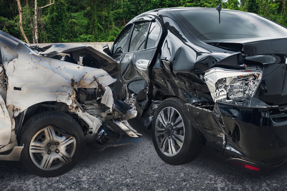 Two severely damaged cars after a collision on a road surrounded by greenery.