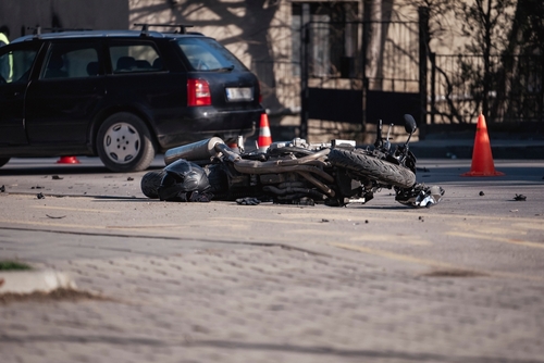 A motorcycle lying on the ground after a collision with a car in an urban setting, with visible debris scattered on the road.