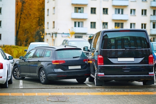 Two cars involved in a minor collision in a parking lot, with one vehicle's rear bumper slightly overlapping the side of the other vehicle.