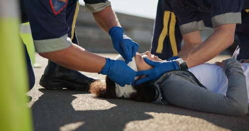 Emergency responders placing a head bandage on an injured woman lying on the ground after an accident.