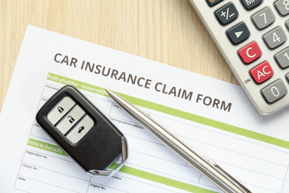 car insurance claim form with car key and calculator on wooden desk