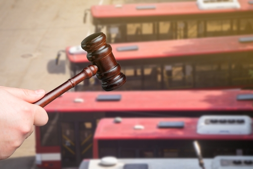 A hand holding a gavel with red buses in the background, symbolizing legal action involving transportation or accident cases.