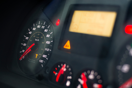 Close-up of a truck dashboard showing warning lights and a speedometer, indicating potential violations of safety regulations.