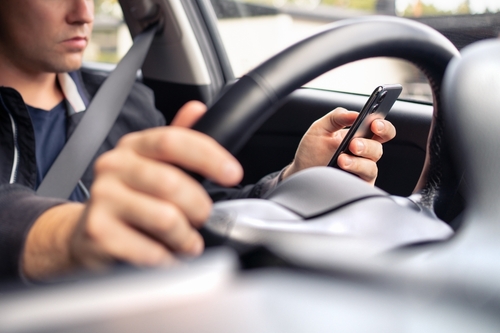 Close-up of a driver holding a smartphone while steering, illustrating distracted driving during a rideshare trip.