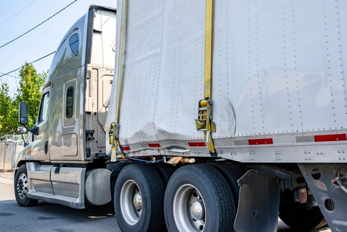 Close-up of a commercial truck with visible dents on its trailer, showing damage sustained in an accident.