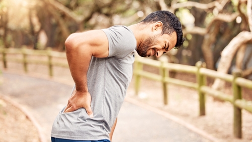 Man outdoors clutching his lower back in discomfort, highlighting the impact of a back injury after an accident or strenuous activity.