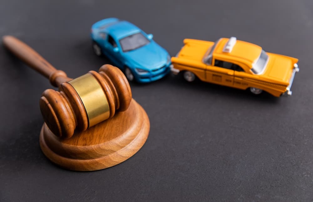 A judge’s gavel positioned in the foreground with two cars colliding in the background, symbolizing a traffic accident case.