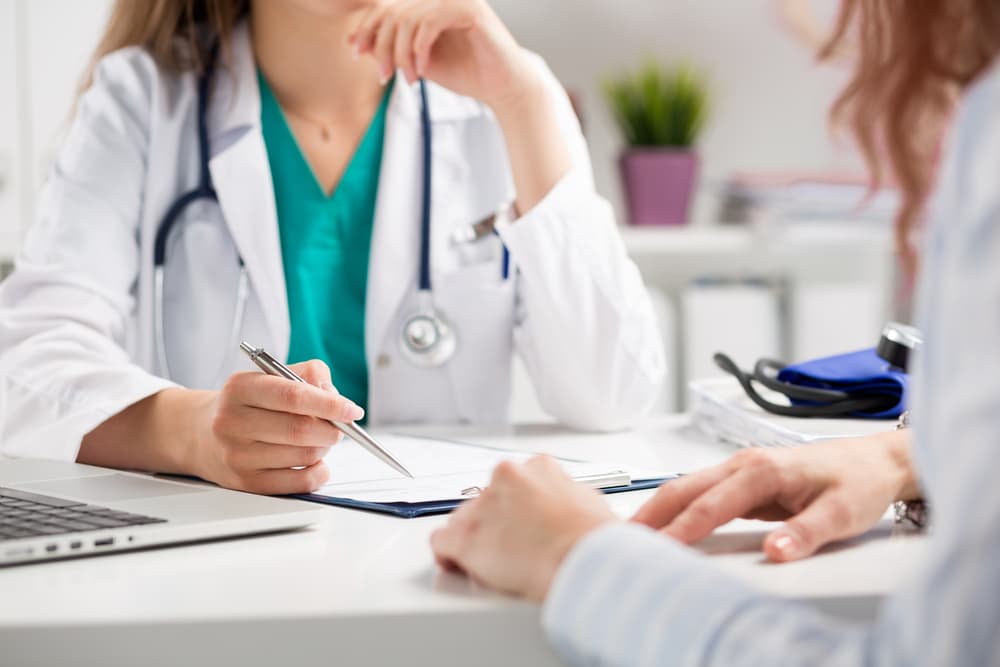 Doctor consulting a patient with a close-up focus on their hands. The patient sits in the doctor’s office during a medical consultation. 