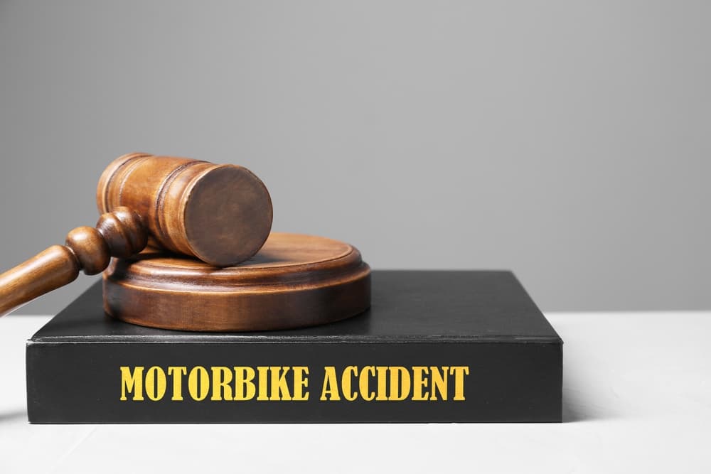 Motorcycle accident law book and judge's gavel on a light-colored table with a gray background, providing space for text.