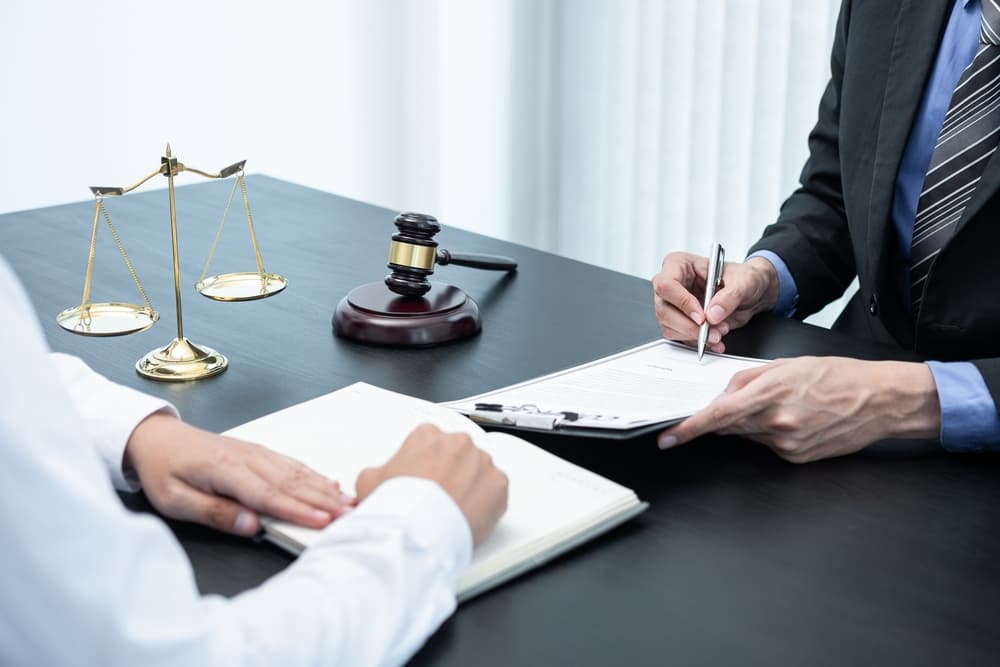 A professional male lawyer or legal counselor discussing a negotiation case with a client, reviewing contract documents in an office setting. Law, justice, attorney services, and lawsuit concepts are represented.