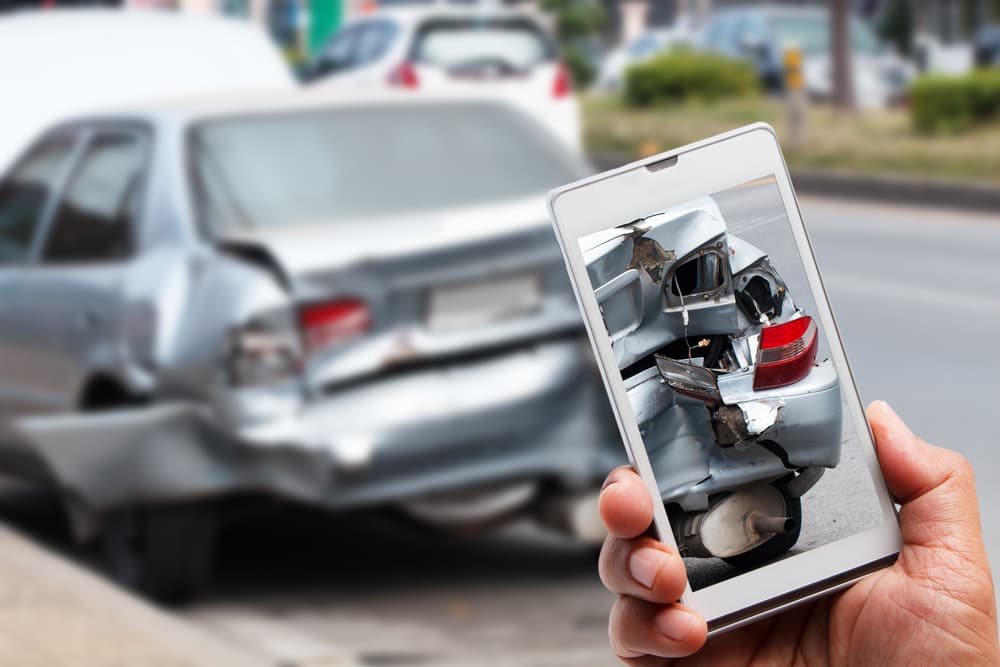 Close-up of a hand holding a smartphone, capturing a photo of a car accident.






