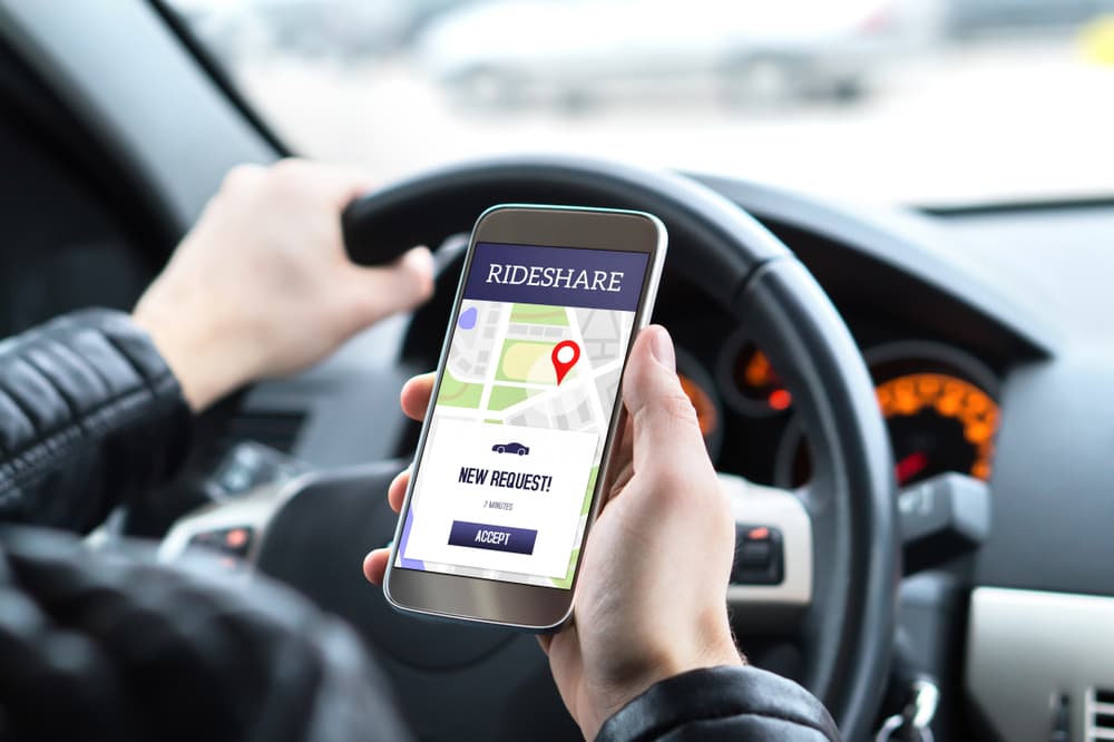 A rideshare driver sits in the car, using a mobile phone app to accept a new ride request. The driver prepares to pick up passengers for an online carpool service.






