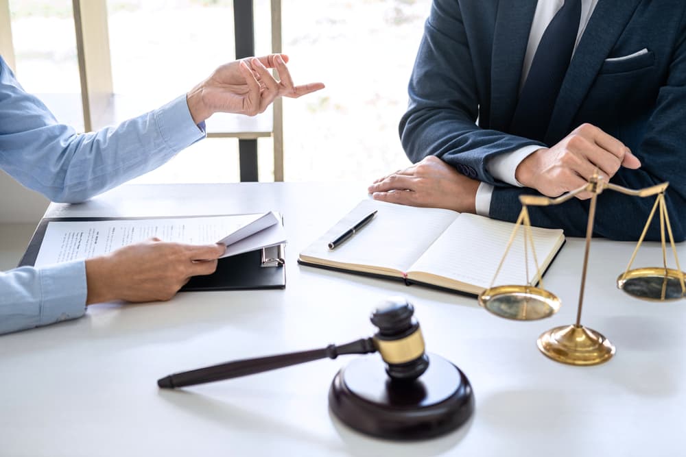 A businesswoman consults with a male lawyer or judge during a team meeting at a law firm office. The discussion focuses on legal matters, highlighting law and legal services.