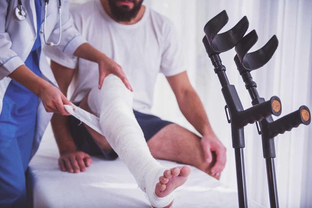 Young man with a leg injury receiving assistance from a female doctor.