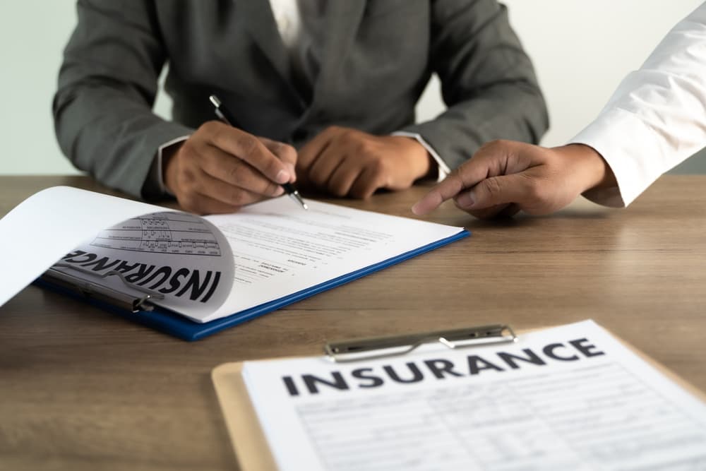 An insurance agent is reviewing a family health insurance policy, examining the details. He is in the process of signing the claim, ensuring everything is in order.






