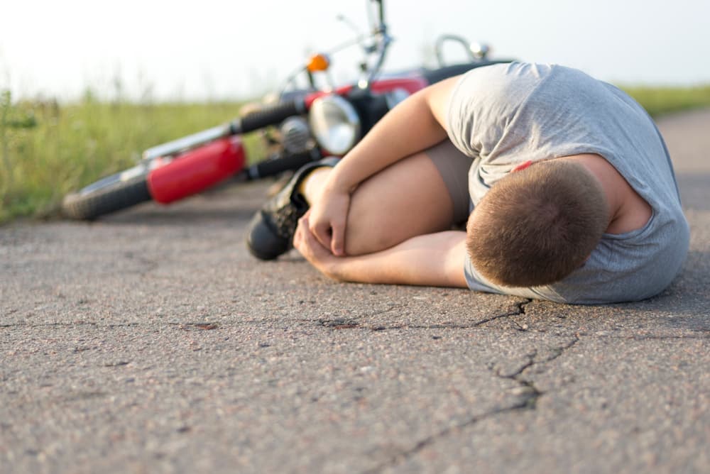 A man clutches his knee while lying on the asphalt next to his motorcycle, illustrating the aftermath of a road accident.