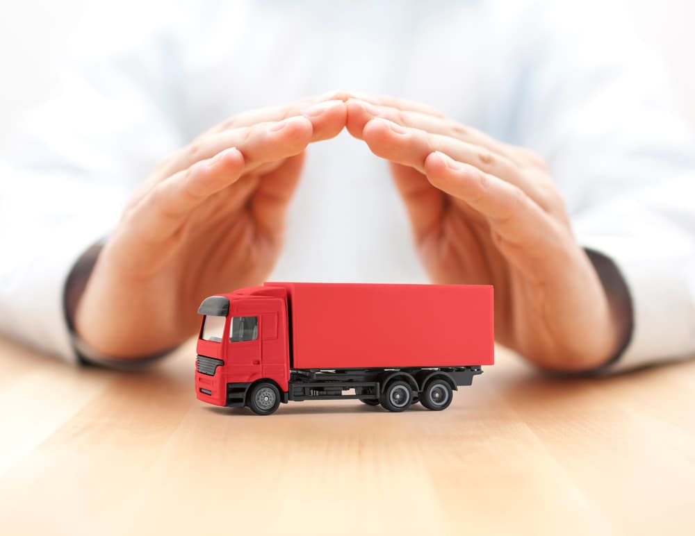 Red cargo delivery truck secured under protective hands, symbolizing safety, insurance, and reliable transport.